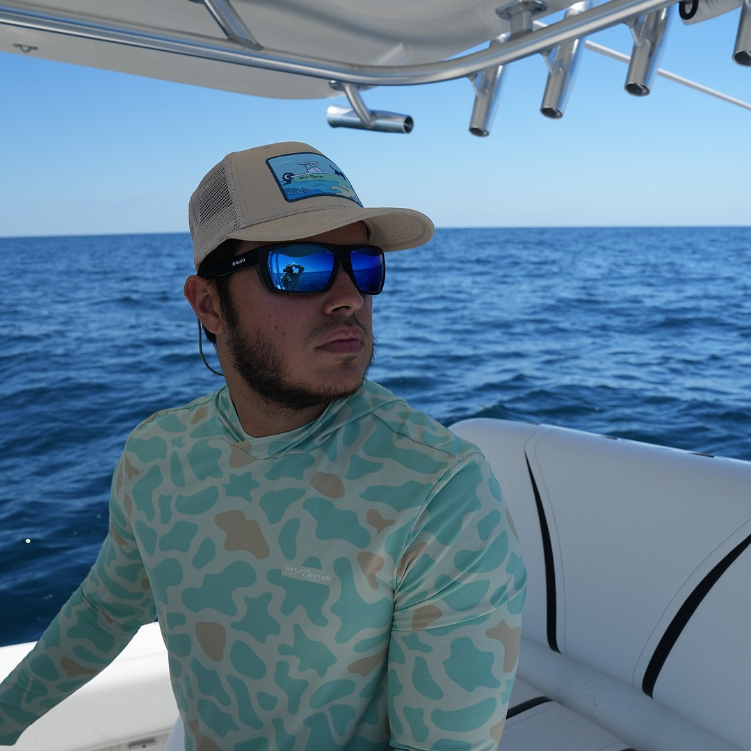 Man seated on a boat in the Wet Water Offshore Original Hoodie, cap and sunglasses — front view