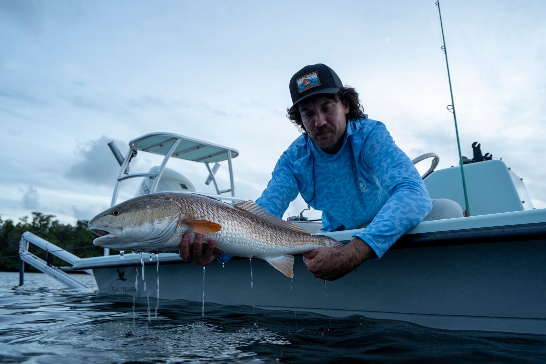 Angler holding a redfish at the gunwale at dusk